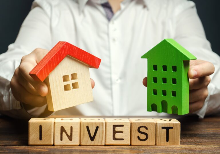 Wooden blocks with the word Invest, and houses in the hands of a businessman. The concept of investing in real estate construction. Effective investment. Buying apartments
